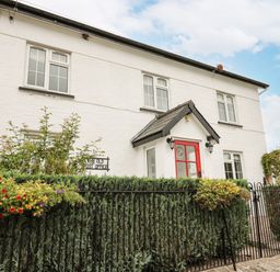 A white two-story house with a red door and iron fence with flower baskets at The Old Post Office in Llandrindod Wells
