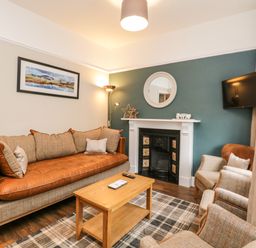 A living room with a sofa armchairs wooden coffee table fireplace and a wall-mounted TV at Netherbeck in Ambleside