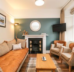 A living room with a brown sofa two armchairs a wooden coffee table a fireplace and a wall mounted TV at Netherbeck in Ambleside