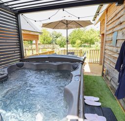 An outdoor hot tub with water bubbling next to a wooden wall with a robe and slippers at Lake View Lodge in Thorpe-On-The-Hill