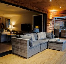 A seating area with cushioned wicker sofas on a wooden deck next to an indoor living room at Lake View Lodge in Thorpe-On-The-Hill