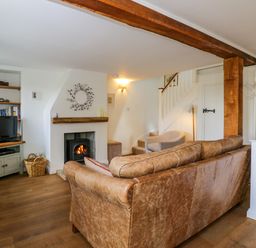 A living room with a leather sofa a fireplace a TV on a cabinet and a staircase at Little Owl Barn in Burford