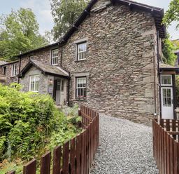 A stone house with a gravel pathway and wooden fence surrounded by greenery at Eller Close House in Grasmere