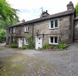 A stone cottage with a gravel driveway at Fellside Cottage in Bowness-On-Windermere