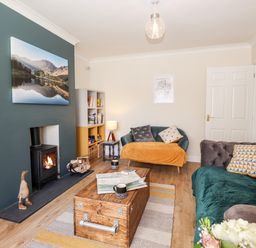 A living room with a wood burning stove paintings sofas and a wooden coffee table at Pooley Howe in Keswick