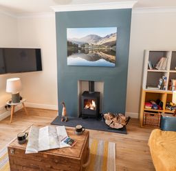 A living room with a fireplace wood stove a TV mounted on the wall a wooden chest a bookshelf and a sofa at Pooley Howe in Keswick