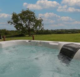 A hot tub with bubbling water outdoors overlooking a green field and a tree at Swallows Nest in Puxey near Sturminster Newton