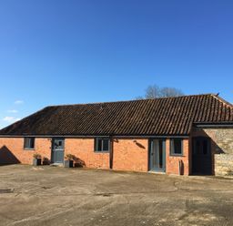 A single-story brick building with a tiled roof and multiple doors and windows at Swallows Nest in Puxey near Sturminster Newton