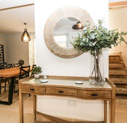 A wooden console table with drawers and a glass vase with foliage next to stairs and a round mirror above at 23 Daniel Street in Bath