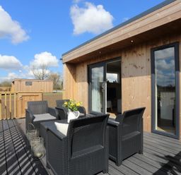 An outdoor wooden deck with black wicker chairs and a table with flowers at The Wren in Wem