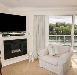 A living room with a large armchair a seahorse cushion a wall-mounted television and glass doors overlooking boats on water at Creekside House in Fowey