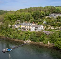 A waterfront house with a dock and boats surrounded by trees and gardens at Creekside House in Fowey
