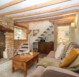 A living room with a sofa and wooden coffee table near a fireplace and a staircase at Tuesday Cottage in Bourton-On-The-Water
