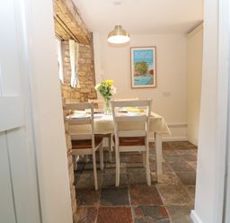 A dining area with a table covered by a yellow and white tablecloth four chairs a vase with flowers and a framed wall poster at Tuesday Cottage in Bourton-On-The-Water