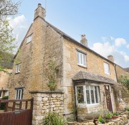 A stone cottage with a wooden gate and potted plants outside at Tuesday Cottage in Bourton-On-The-Water