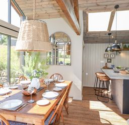 A dining area with a wooden table set for six and a kitchen island with stools under skylights at The Owl's Shack in Kendal