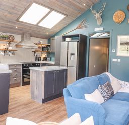 A kitchen with wooden cabinets, island, stainless steel refrigerator, stove, and a blue couch with cushions at The Owl's Shack in Kendal