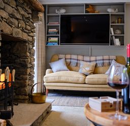 A living room with a stone fireplace a beige sofa and a mounted television at The Old Water Mill in Kendal
