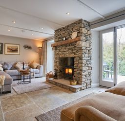 A living room with a stone fireplace sofas tables and glass doors at The Old Water Mill in Kendal
