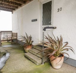 A covered entrance with steps two potted plants a wooden bench and a door labeled sandy toes at Rhosneigr