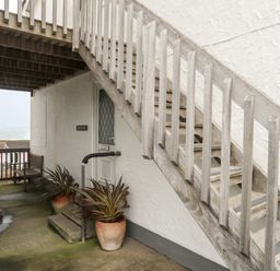 An outdoor stairway with wooden railings next to a white door with potted plants underneath at Sandy Toes in Rhosneigr