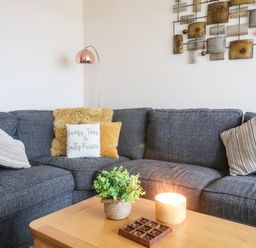 A corner sofa with cushions a coffee table with a plant a lit candle and a tic tac toe game in a living room at Sandy Toes in Rhosneigr