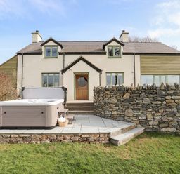 A backyard patio with a hot tub stone wall and a two-story house in the background at Dolwaenydd in Brynsiencyn