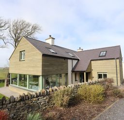 A modern house with stone wall and large windows surrounded by grass and trees at Dolwaenydd in Brynsiencyn