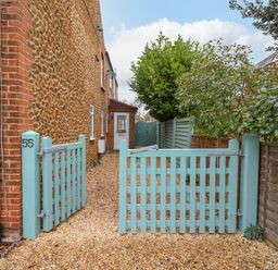A gravel driveway with a light blue wooden gate leading to a door on a stone and brick house at Job's Cottage in Snettisham