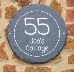 A round house number plaque with the number 55 and the name Jobs Cottage on a brick wall at Jobs Cottage in Snettisham