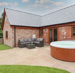 An outdoor patio with a wicker sofa set and a hot tub next to a brick house at The Clockhouse in Llandyssil near Montgomery