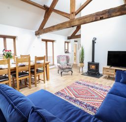 A living room with a blue sofa a colorful rug a wooden dining table and chairs a patterned armchair a plant a wood stove and a television at The Clockhouse in Llandyssil near Montgomery