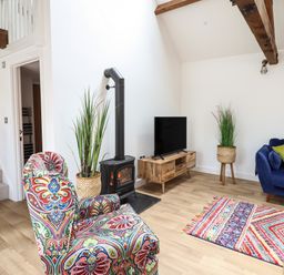 A living room with a colorful armchair a wood stove and a television on a wooden stand at The Clockhouse in Llandyssil near Montgomery