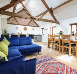 An open living and dining area with blue sofas and colorful rug and wooden dining table at The Clockhouse in Llandyssil near Montgomery