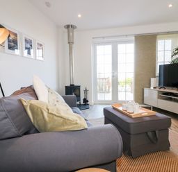 A living room with a gray sofa and cushions a floor lamp stove coffee table TV and sliding glass doors at Badgers Way in Tintagel