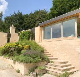 A modern house with large windows and steps surrounded by shrubs and trees at Under Catswood in Elcombe near Stroud
