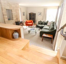 A living room with a green sofa an orange armchair a glass coffee table a fireplace and wooden stairs at Under Catswood in Elcombe near Stroud