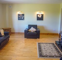 A living room with black leather sofas floral cushions wooden flooring and a fireplace at Tra Gheal in Kilmore County Wexford