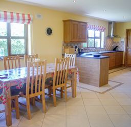 A kitchen with a dining table and wooden chairs near windows with striped blinds at Tra Gheal in Kilmore County Wexford