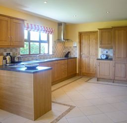 A kitchen with wooden cabinets tiled floor and a window with a striped blind at Tra Gheal in Kilmore County Wexford