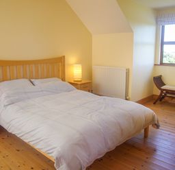 A bedroom with a wooden bed frame bedside tables with lamps a window and a bench at Tra Gheal in Kilmore County Wexford