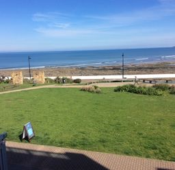 A grassy park area with benches and a walking path near a rocky beach and ocean at The Lobster Pot in Westward Ho