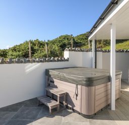 An outdoor hot tub with steps on a patio next to a white house at Haul A Gwynt in Criccieth
