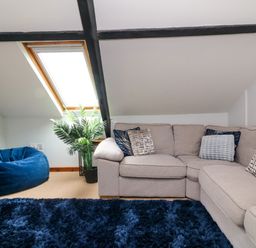 A living room with a beige sectional sofa with pillows a blue bean bag a plant under a skylight window and a blue shaggy rug at Horseshoe Cottage in Hartland
