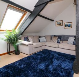 A corner sofa with cushions near slanted ceiling window and black beams in a living room at Horseshoe Cottage in Hartland
