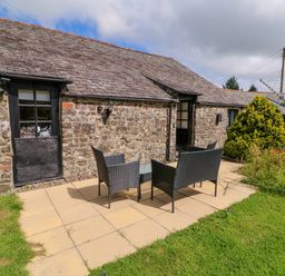 An outdoor seating area with a table and four chairs on a patio beside a stone cottage with a sloped roof at Horseshoe Cottage in Hartland