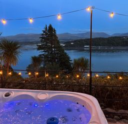 An outdoor hot tub overlooking a river with decorative lights at Afallon in Menai Bridge