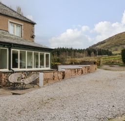 A gravel driveway beside a house with outdoor chairs and a table near a countryside hill at Glen Cottage in Troutbeck near Keswick