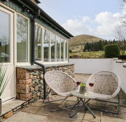 A patio with two woven chairs and a small round table with drinks outside a house at Glen Cottage in Troutbeck near Keswick