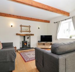 A living room with two gray sofas a wood burning stove a tv on a stand and wooden ceiling beams at Glen Cottage Troutbeck near Keswick